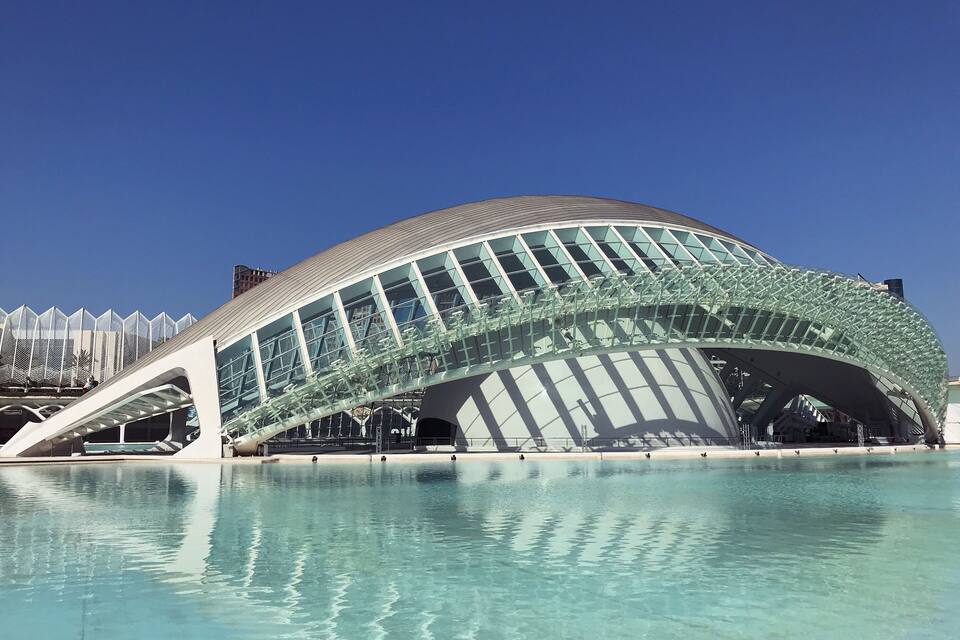 Uma estrutura arquitetônica moderna com fachada de vidro e piscina em primeiro plano.