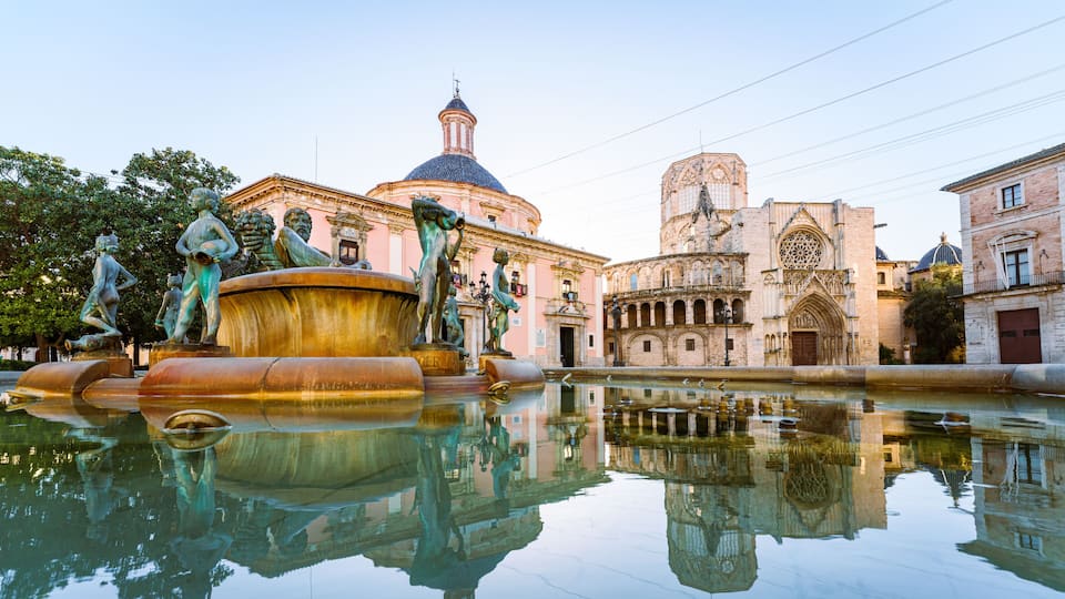 A historic fountain with statues, a domed building, and a cathedral with a rose window.