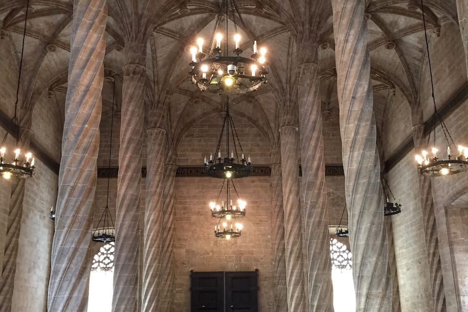 A grand hall with high vaulted ceilings, large stone columns, and ornate chandeliers.