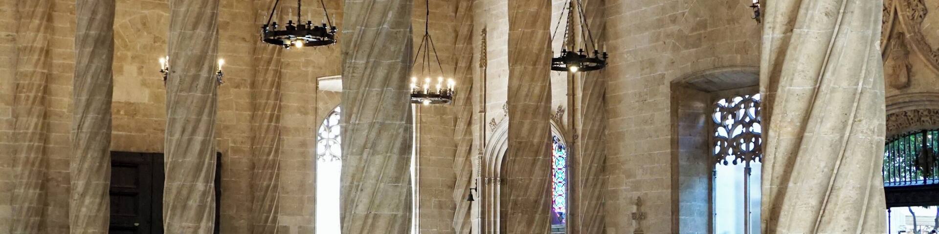 Un gran salón con techos abovedados altos, amplias columnas de piedra y candelabros ornamentados.