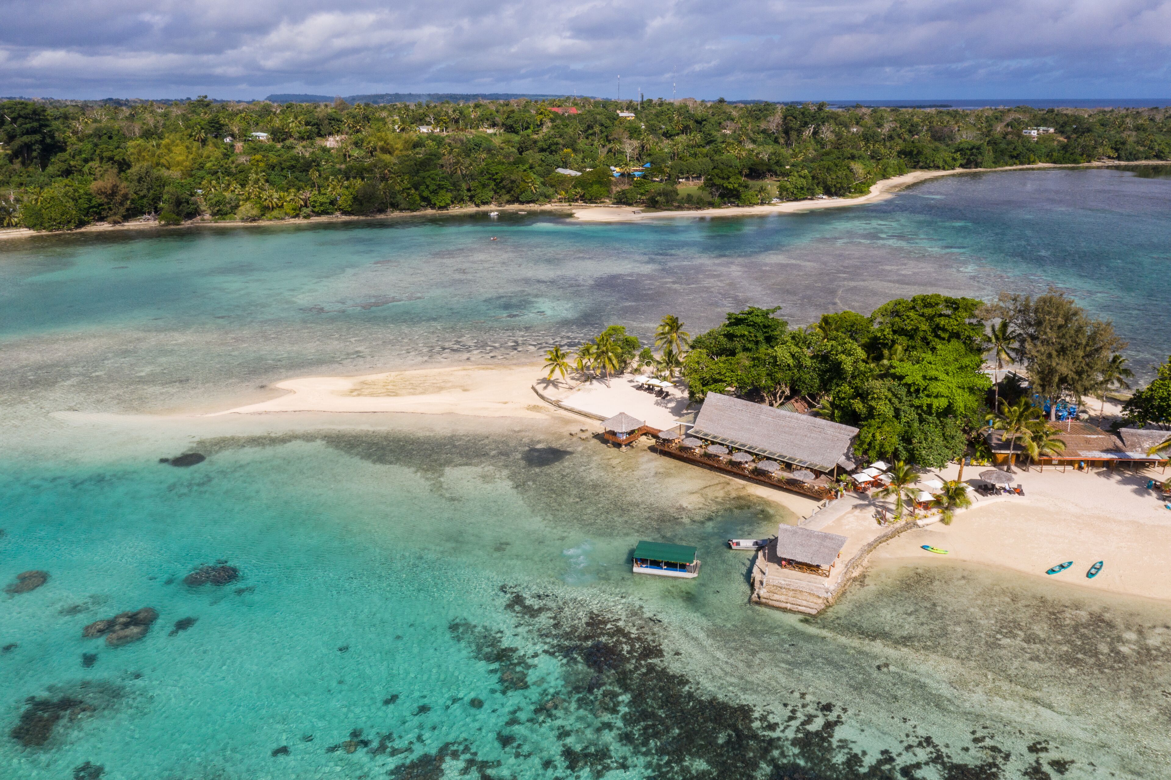 A tropical beach with clear turquoise waters, a sandy shore, and a small resort with palm trees.
