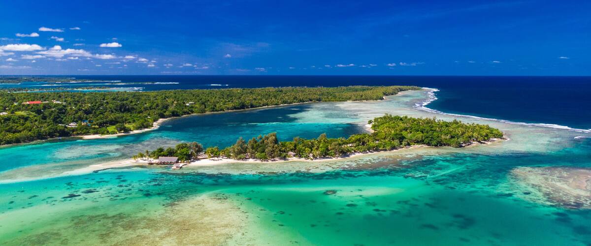 A tropical island with clear turquoise waters, dense green vegetation, and a sandy beach.
