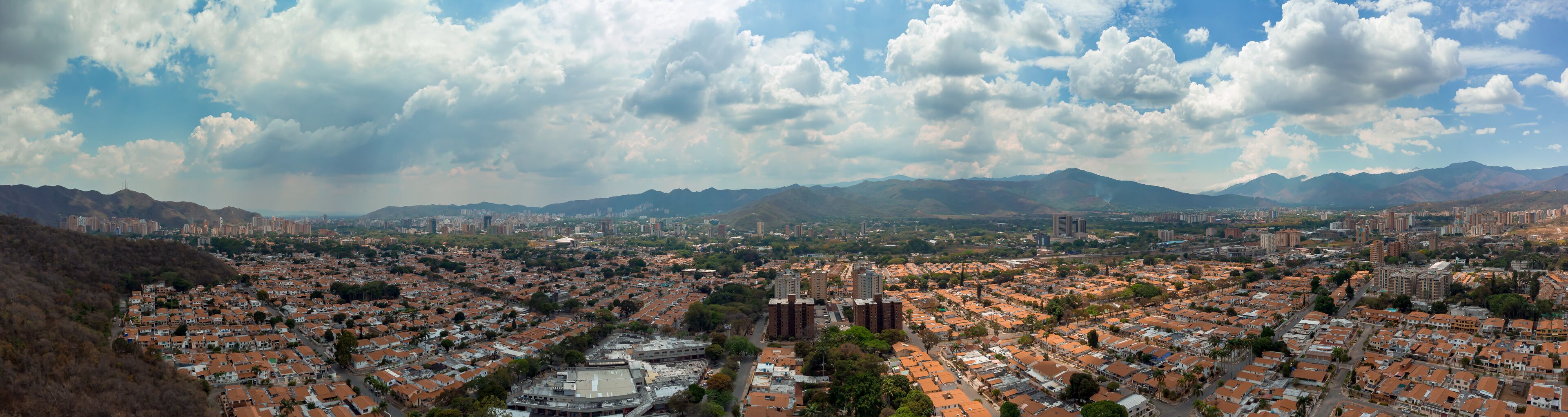 A panoramic view of a city with dense residential areas, a central plaza, and mountains in the background.