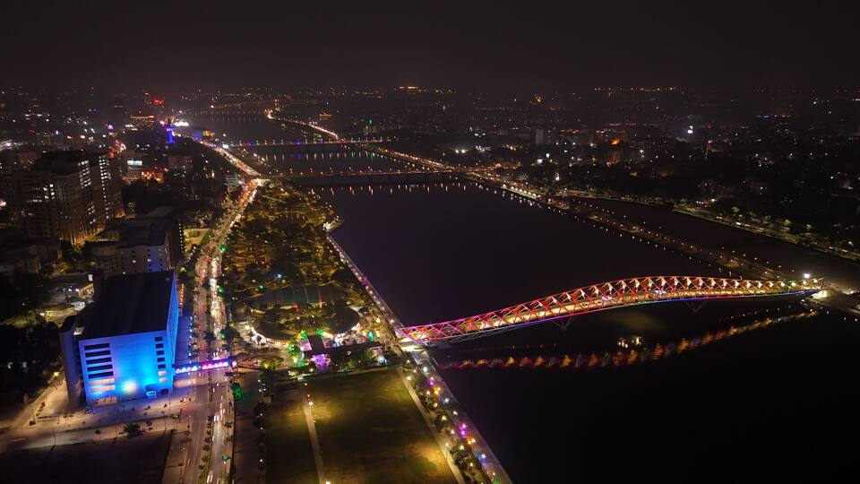 A cityscape at night with a brightly lit bridge spanning a river, surrounded by illuminated buildings and streets.