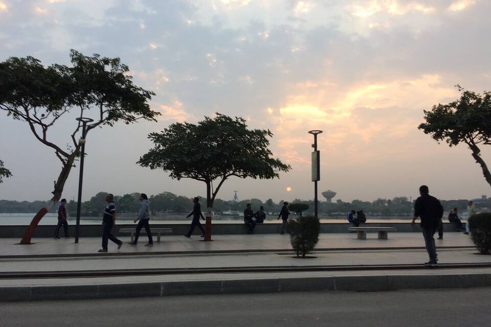 A park with walking paths, trees, benches, and a body of water in the background.