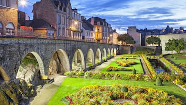 Un puente de piedra con arcos, edificios históricos y un jardín bien cuidado con flores de colores.