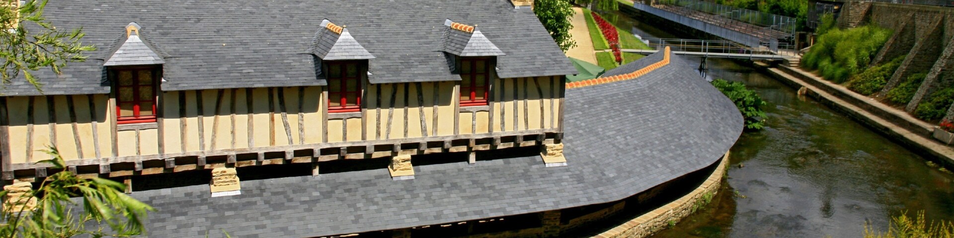 A riverside building with a curved roof, a stone wall, and a bridge in the background.