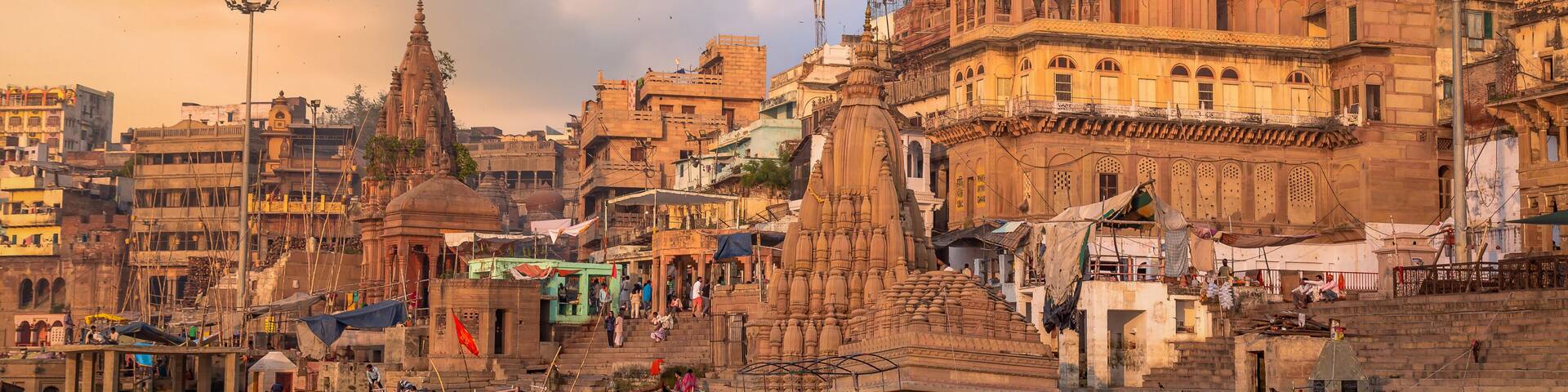 Varanasi city with old architectural buildings and temples along the Ganges river ghat as viewed from a boat at sunset.