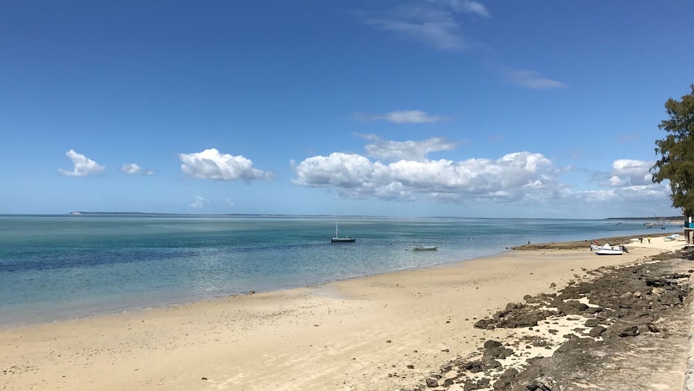 A beach with clear turquoise water, a sandy shore, and scattered rocks.