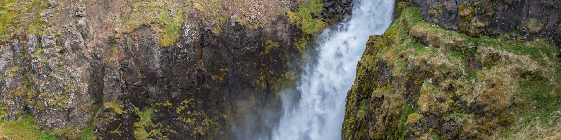 Una cascada se precipita por un acantilado rocoso rodeado de vegetación verde.