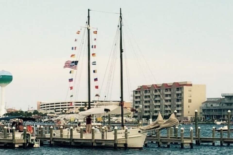 A harbor with a docked sailboat, a building with multiple flags, and a cityscape in the background.