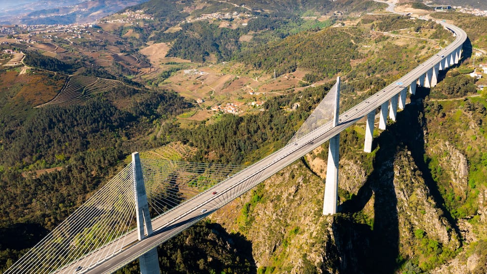 A cable-stayed bridge spanning a deep valley with terraced fields and a distant town.