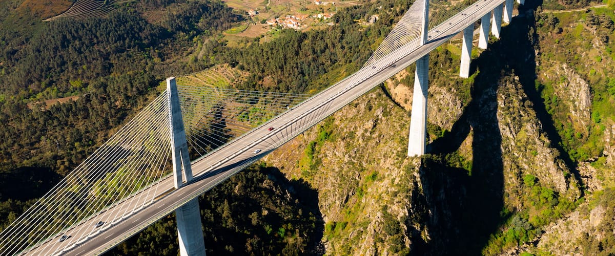 A cable-stayed bridge spanning a deep valley with terraced fields and a distant town.