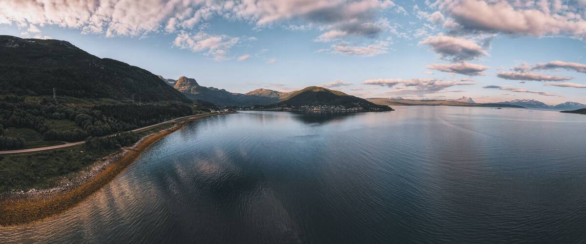 A calm lake surrounded by mountains and a road along the shore.