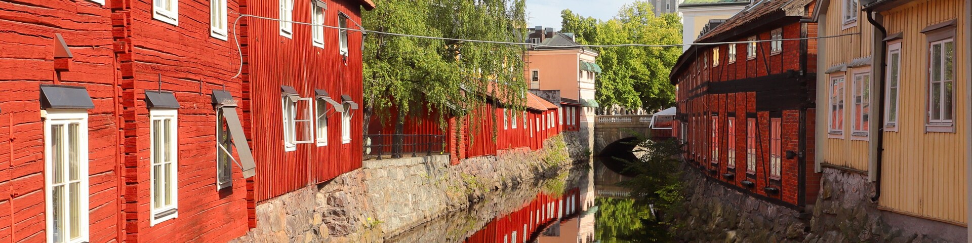 Un canal estrecho con edificios rojos en un lado y un edificio amarillo en el otro, reflejándose en el agua.