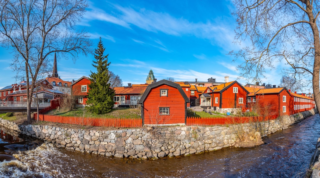 Een rood houten gebouw met een stenen muur en een rivier ervoor.