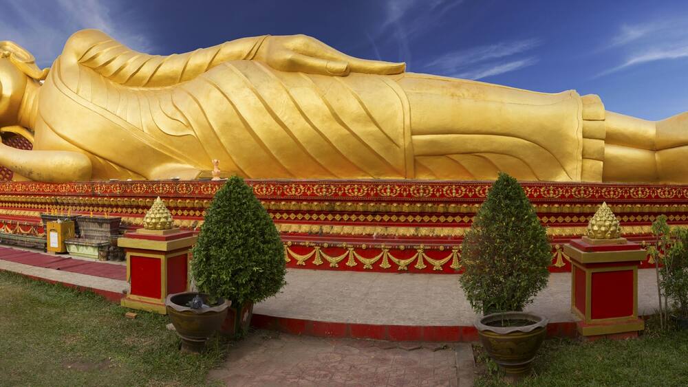 Wide Panoramic View of Reclining Gold Covered Buddha Statue or the Great Stupa, a sacred Buddhist Monument in Pha That Luang, Vientiane, Laos Capital