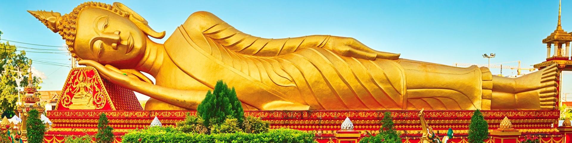 A large golden reclining Buddha statue surrounded by lush greenery and traditional architecture.