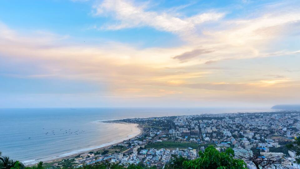 A coastal cityscape with a beach, dense urban area, and a distant mountain range.