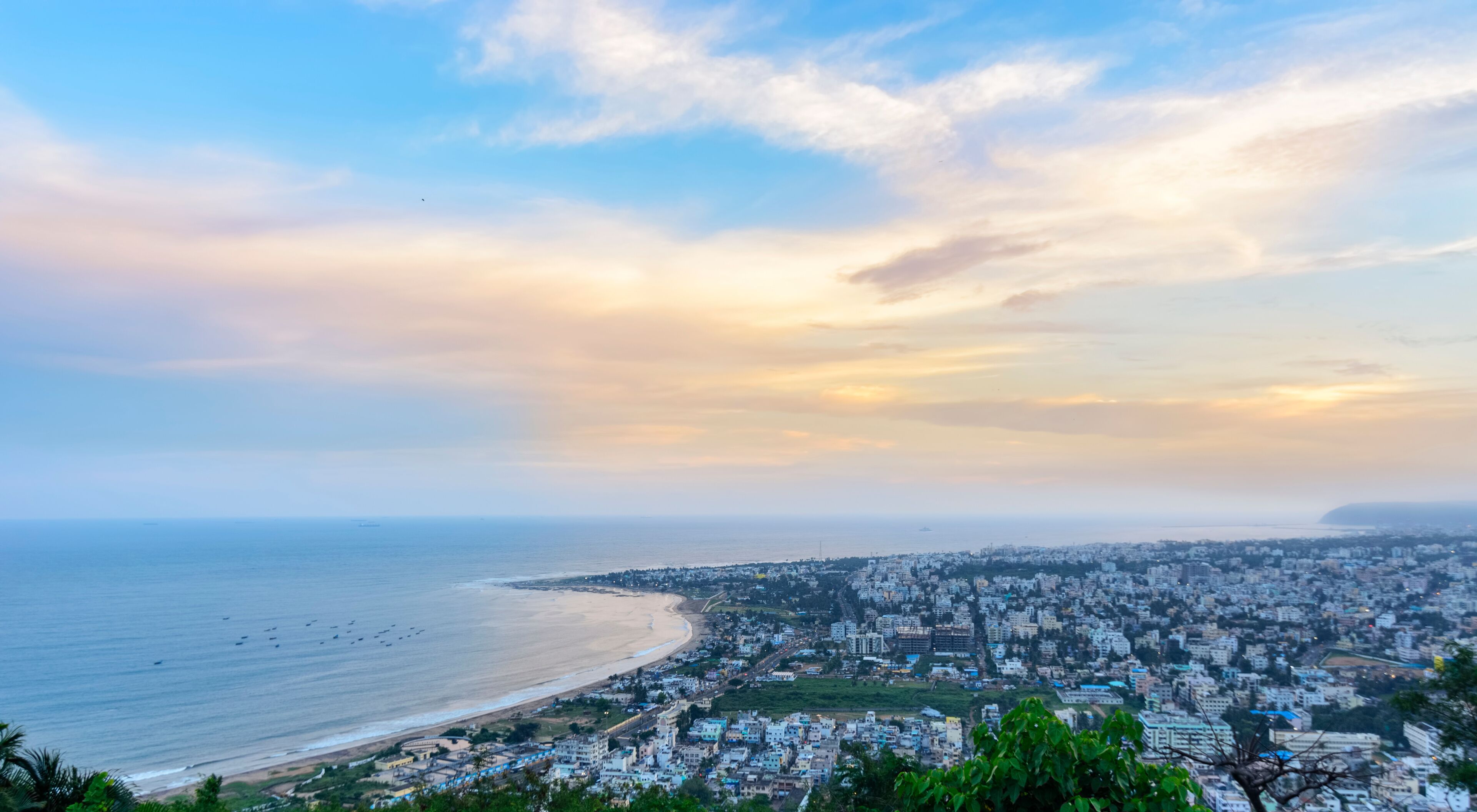 A coastal cityscape with a beach, dense urban area, and a distant mountain range.