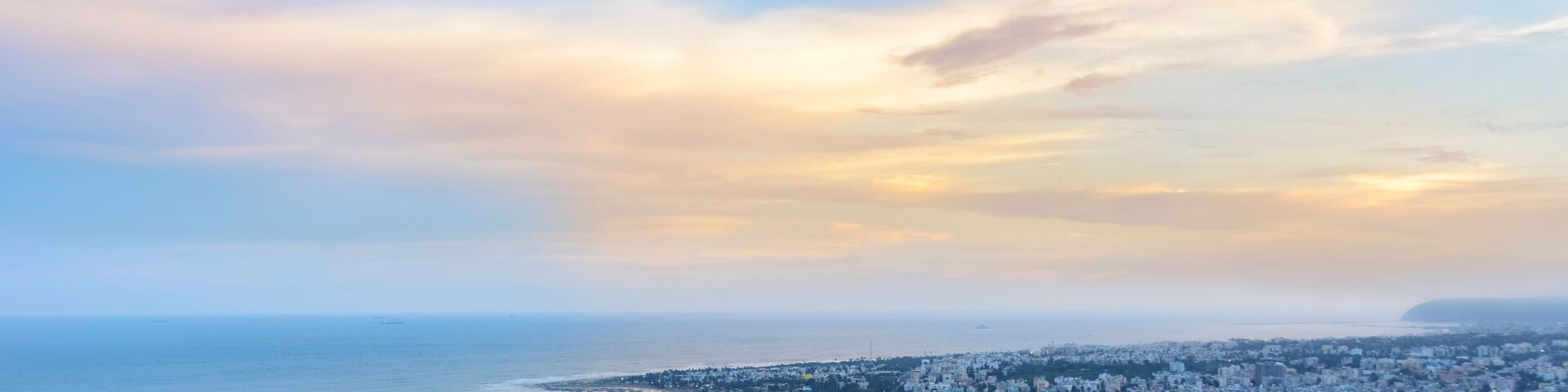 A coastal cityscape with a beach, dense urban area, and a distant mountain range.