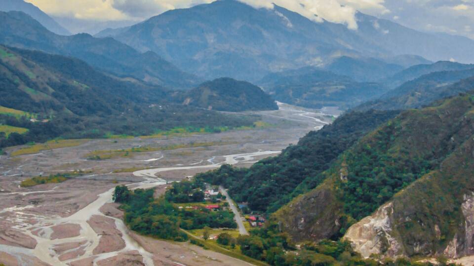 A river winding through a mountainous valley with a village and a large mountain in the background.