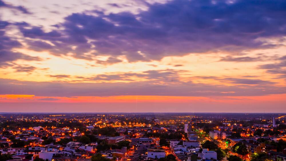 A cityscape at dusk with a sunset sky, illuminated streets, and distant buildings.