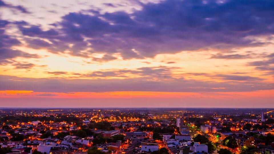 A cityscape at dusk with a sunset sky, illuminated streets, and distant buildings.