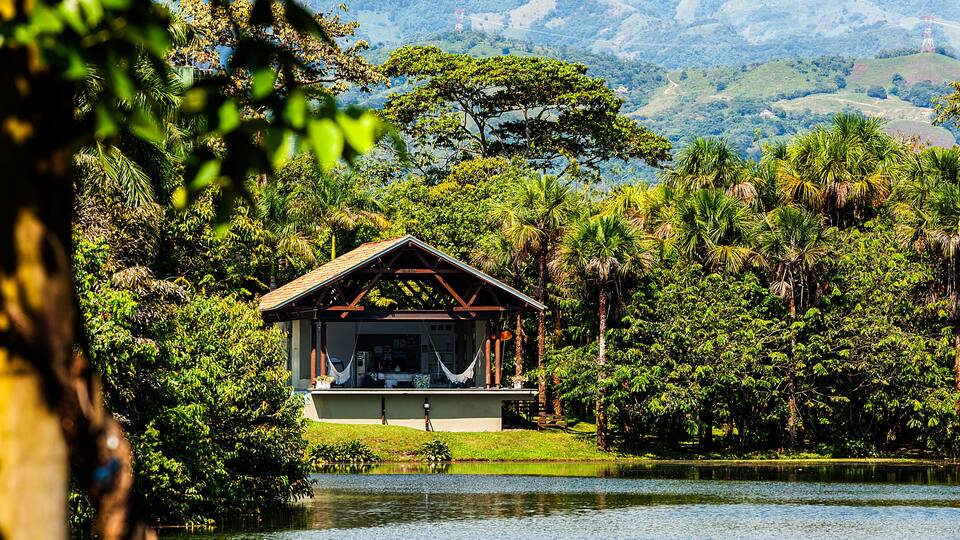 A house by a lake surrounded by lush greenery and hills.
