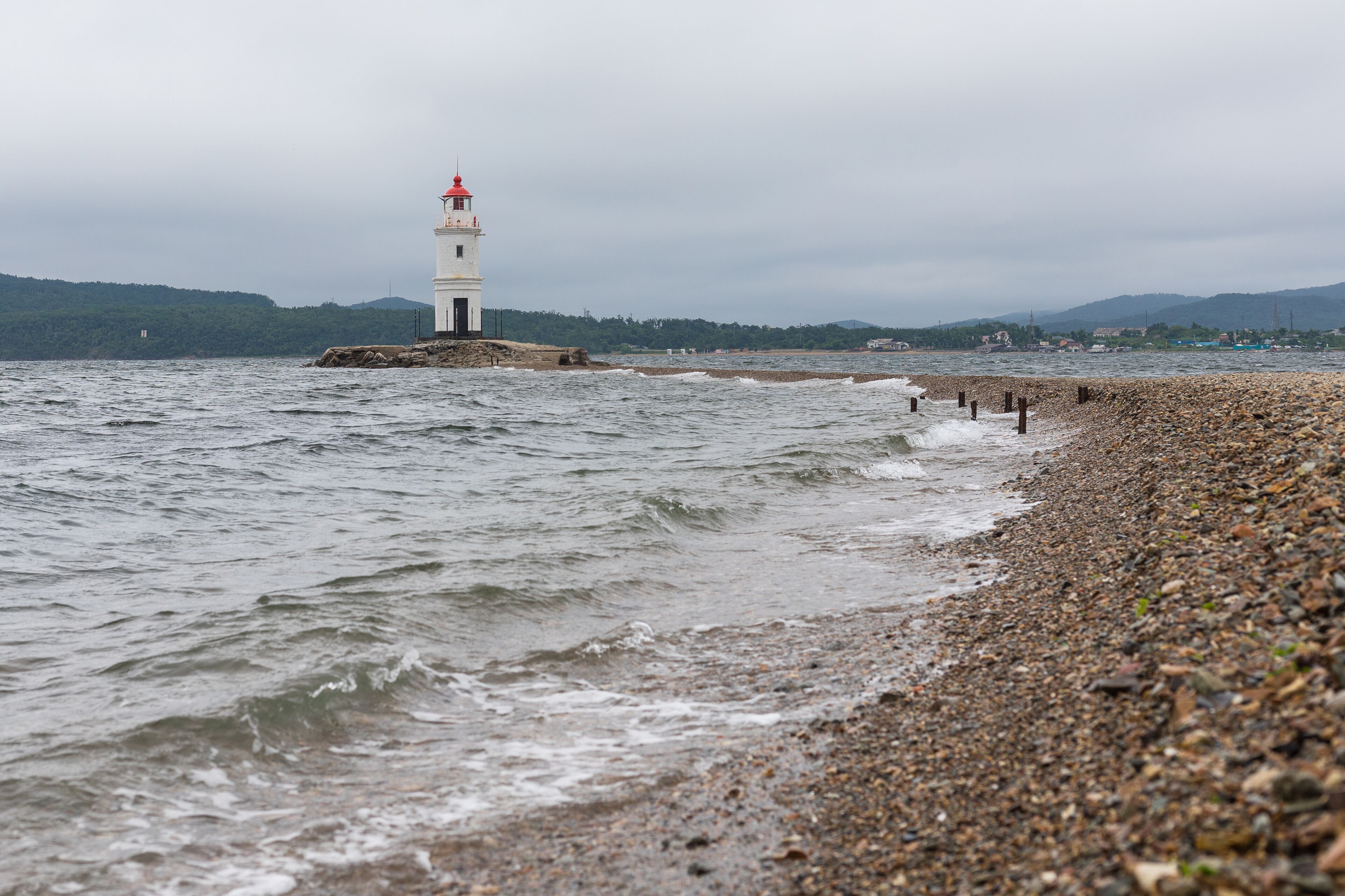 An old lighthouse with a red roof on the seashore. Seascape with copy space. Postcard from travel. Tokarevsky Lighthouse. Vladivostok, Russia.