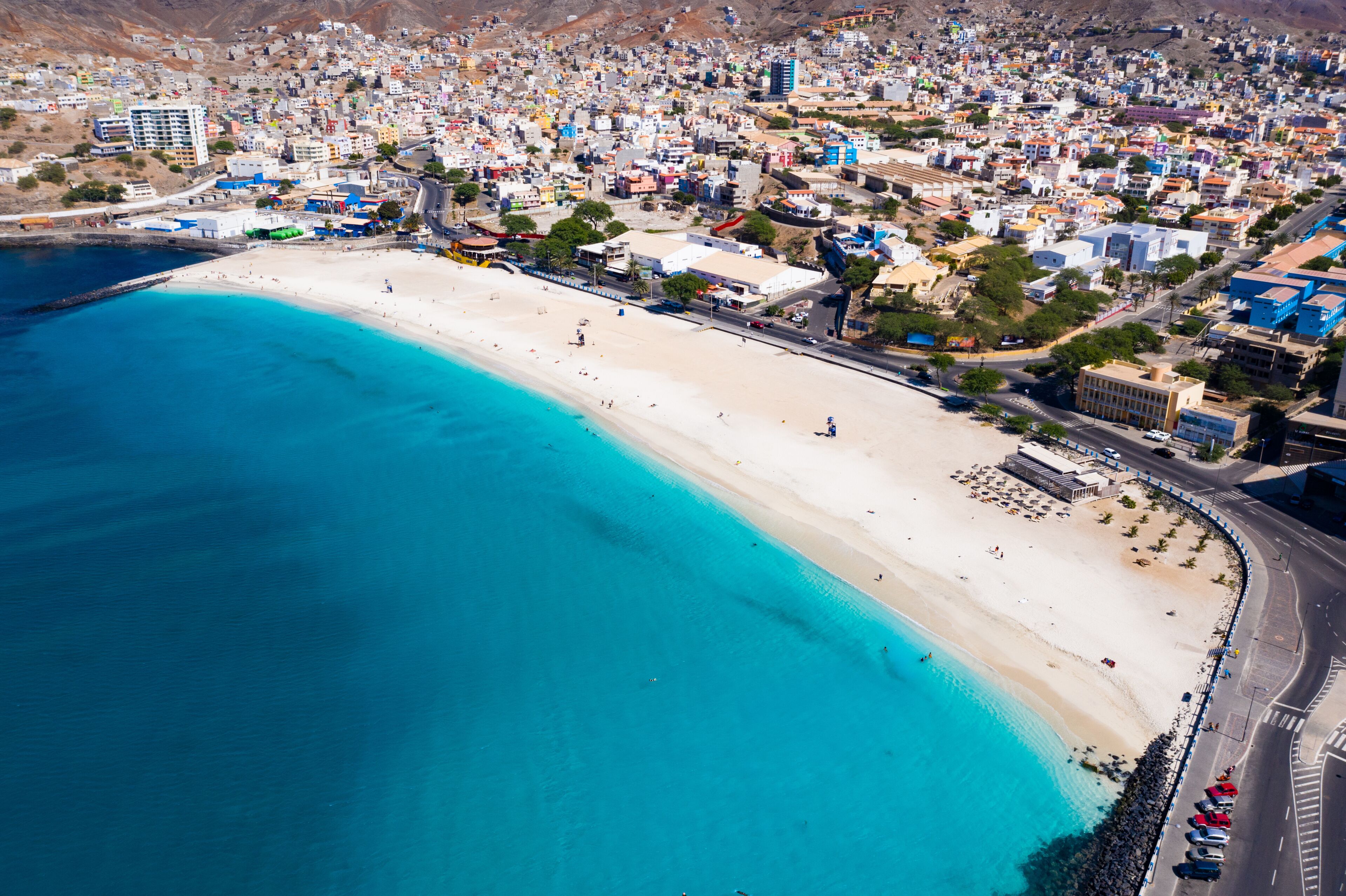 A coastal city with a wide sandy beach, a clear blue sea, and densely packed buildings.