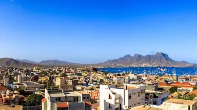 Un paisaje costero con un puerto deportivo, montañas al fondo y un cielo azul despejado.