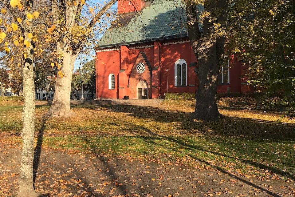 Een rode kerk met een groen dak, omringd door bomen en vallende bladeren.