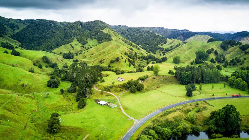A lush green valley with rolling hills, a winding road, a small building, and a river.