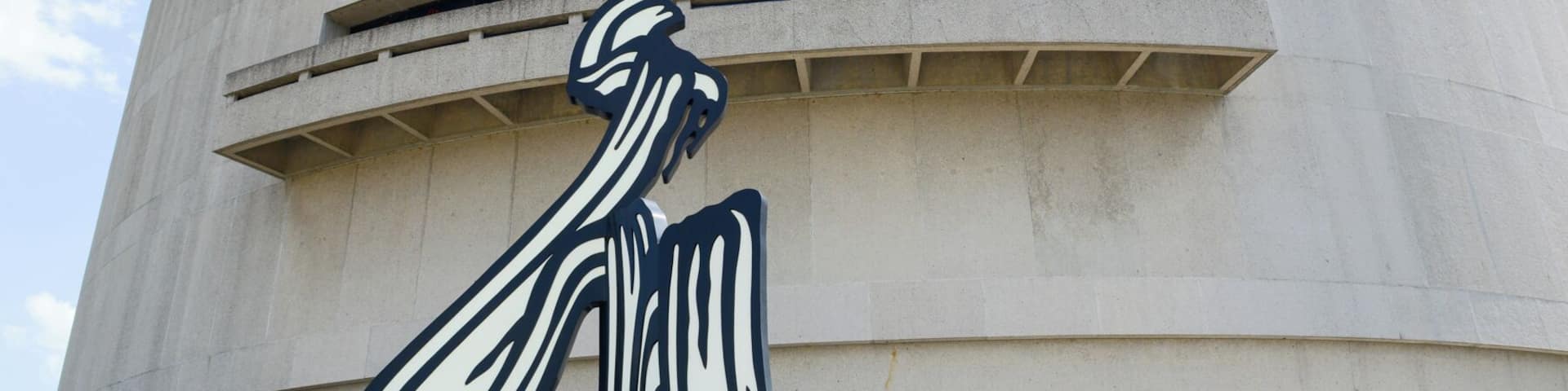 Un grand bâtiment en béton aux formes courbes, sur lequel se trouve une sculpture marquante en noir et blanc représentant une figure humaine.