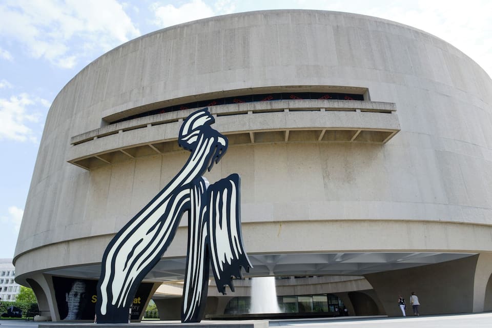 A large, curved concrete building with a prominent black and white sculpture of a figure.