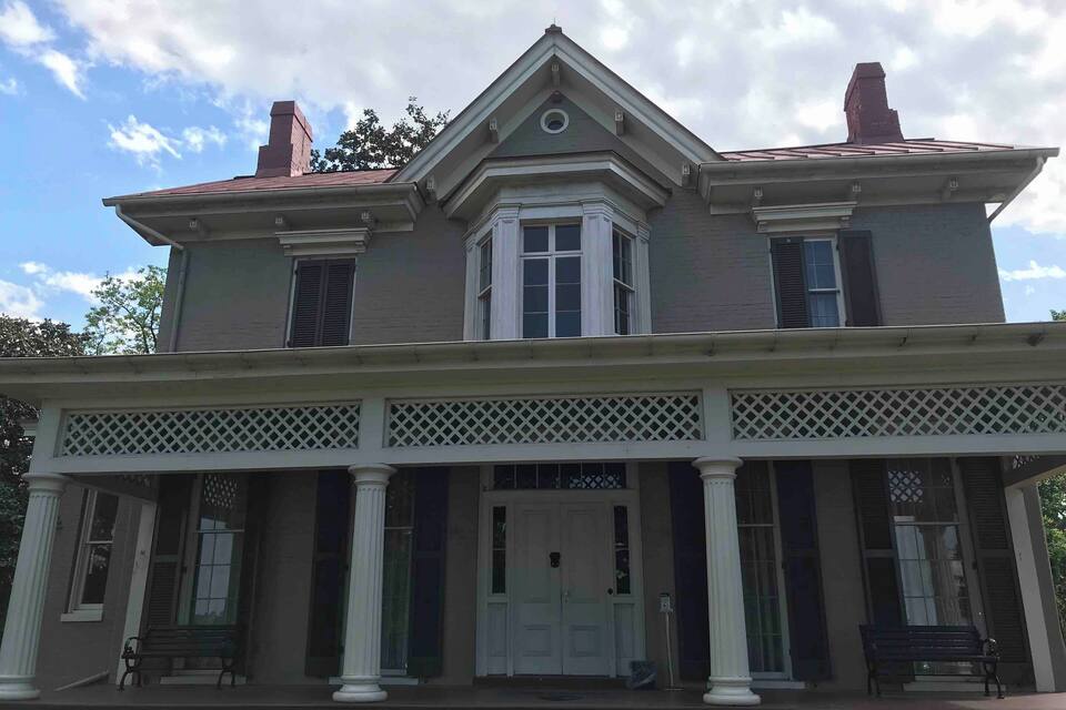Une maison à deux étages dotée d’un porche, de colonnes et de volets.