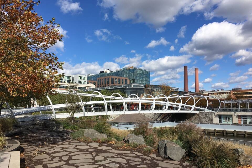 Un chemin de pierre, un pont blanc, des feuilles d’automne et des bâtiments industriels avec des cheminées.