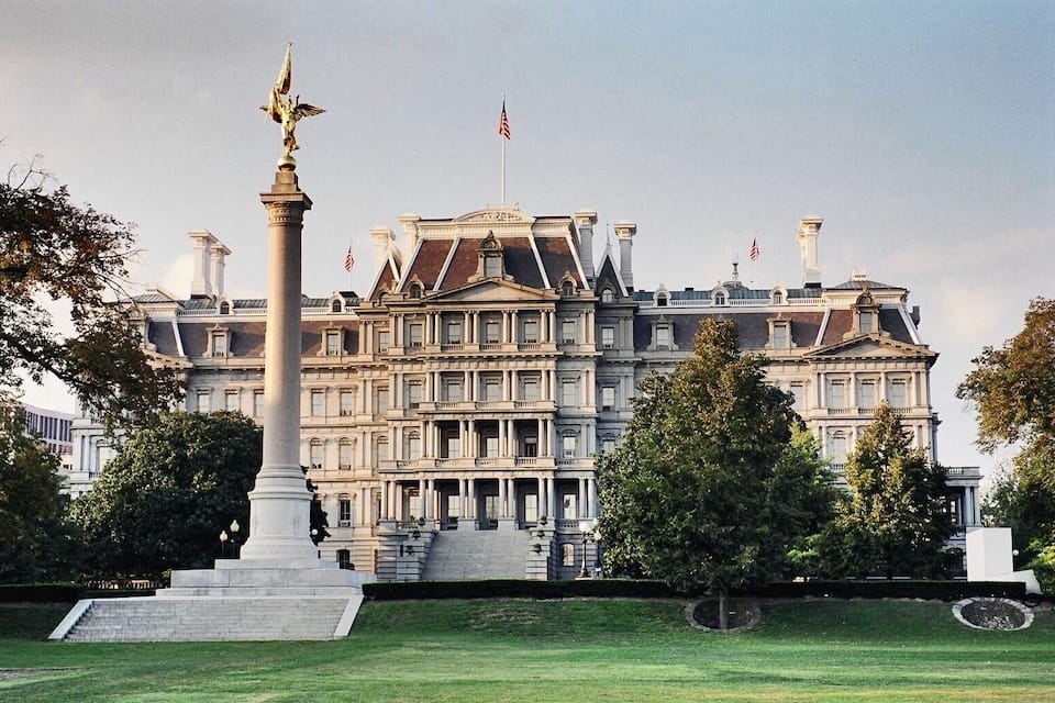 A grand building with a statue in front, surrounded by trees and grass.