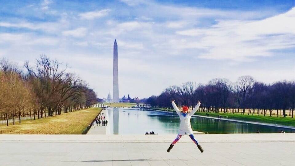 A person jumping in front of the Washington Monument with a river and trees in the background.