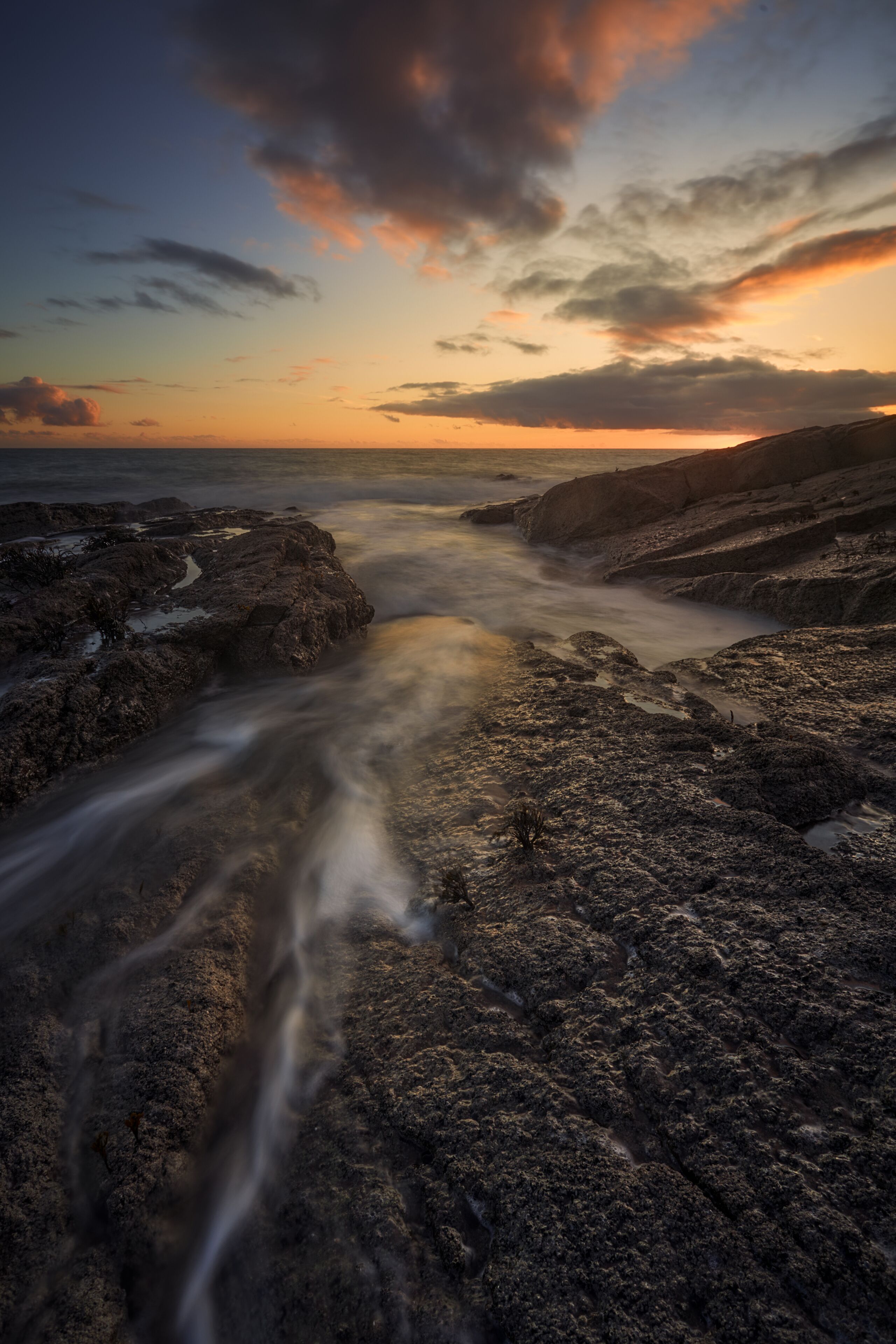 A rocky coastline with a river flowing through it, under a sunset sky.