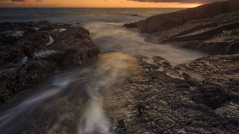 A rocky coastline with a river flowing through it, under a sunset sky.