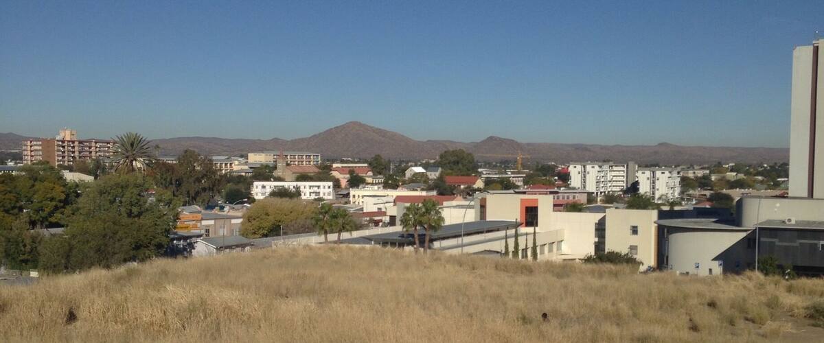 A cityscape with buildings, a clear sky, and distant mountains.