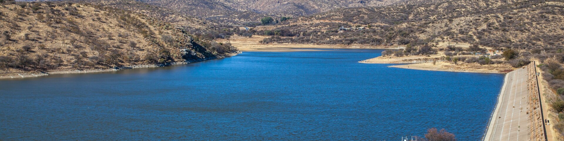 Un río con montañas al fondo y una presa de hormigón a la derecha.