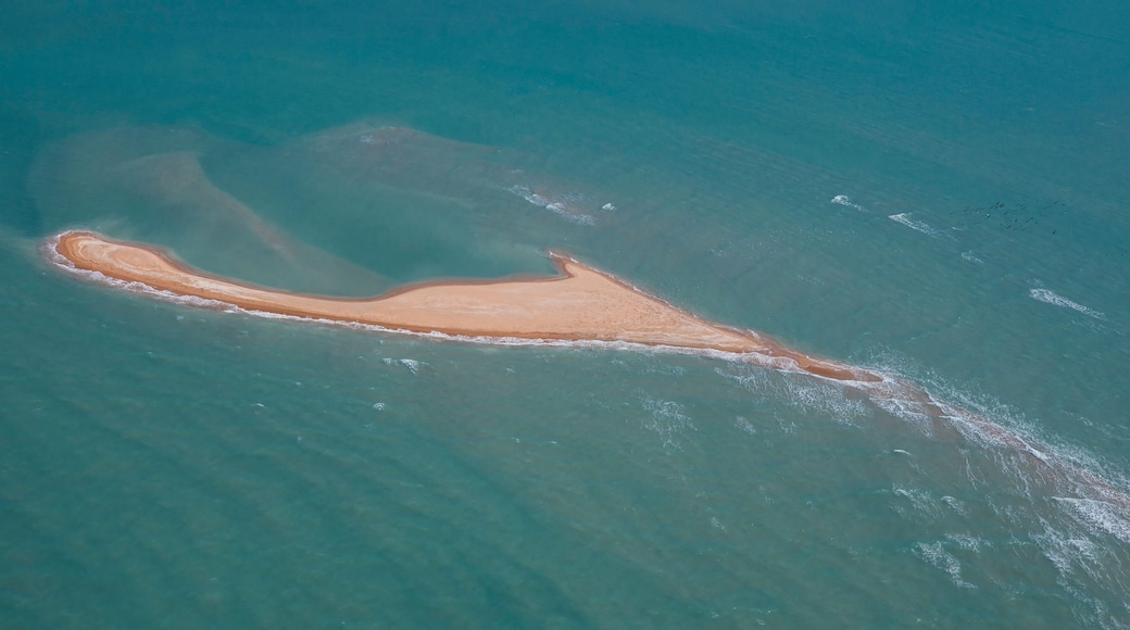 An aerial view of a narrow, elongated island with a sandy beach and clear blue waters.
