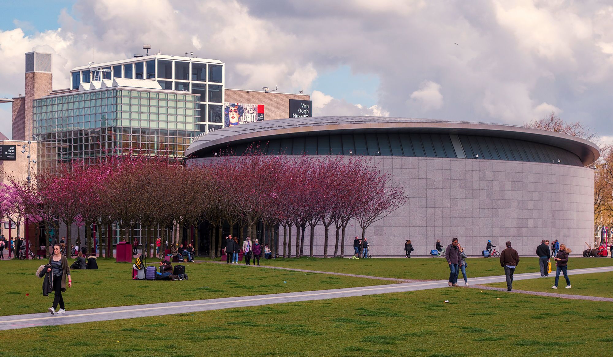 En park med körsbärsträd, en modern byggnad med en glasfasad och en skylt som visar vägen till Van Gogh-museet.
