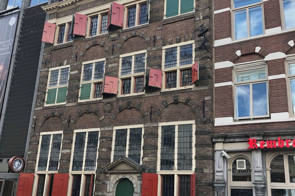 A historic building with red shutters and a green door, featuring classic architecture and a sign for 'Rembrandt'.