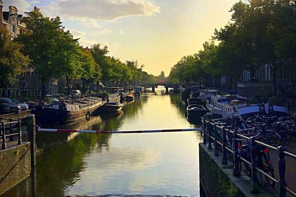 A canal with boats, a bridge, and trees lining the water.