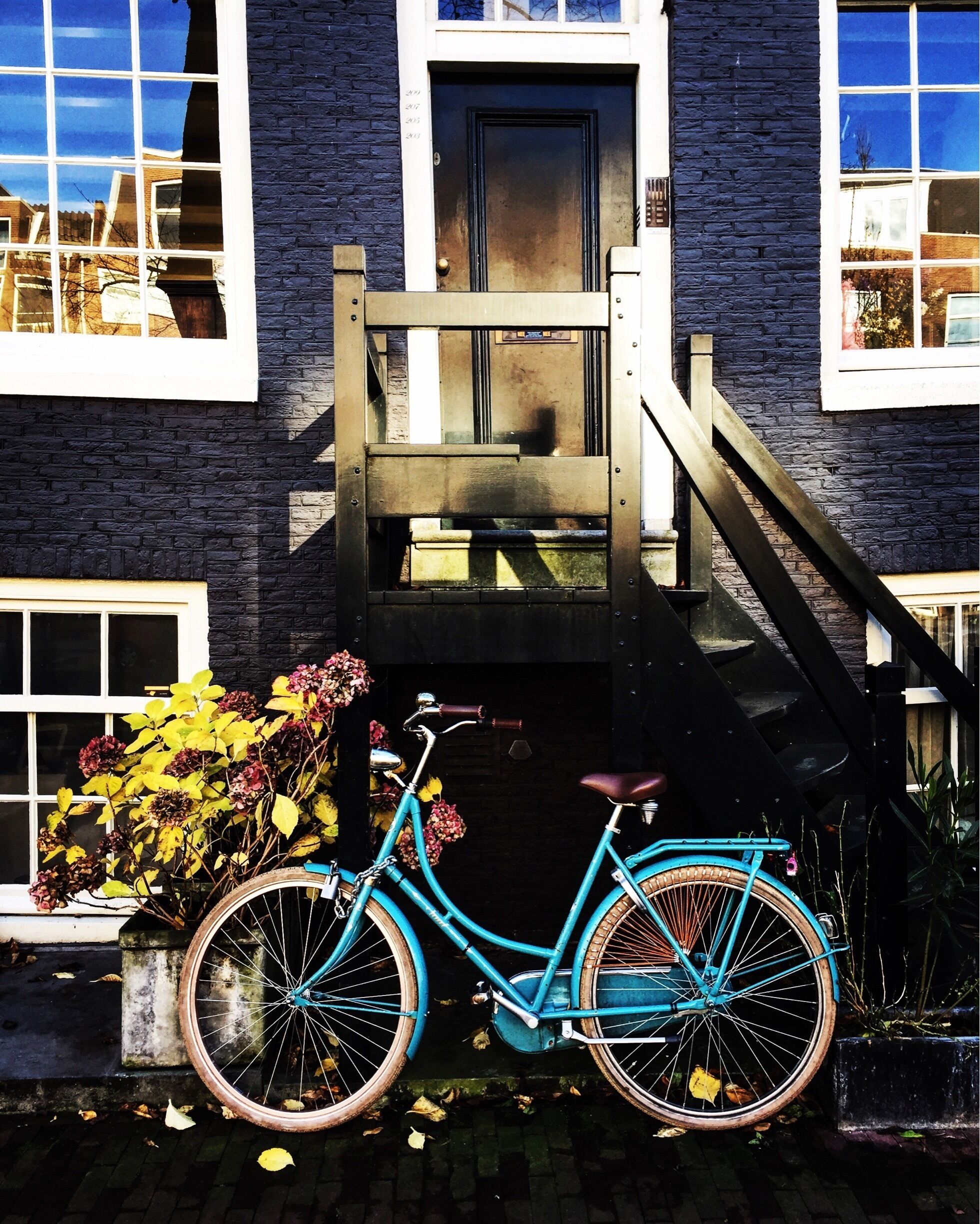 Un vélo turquoise est garé devant une maison dont la porte et la fenêtre sont noires.