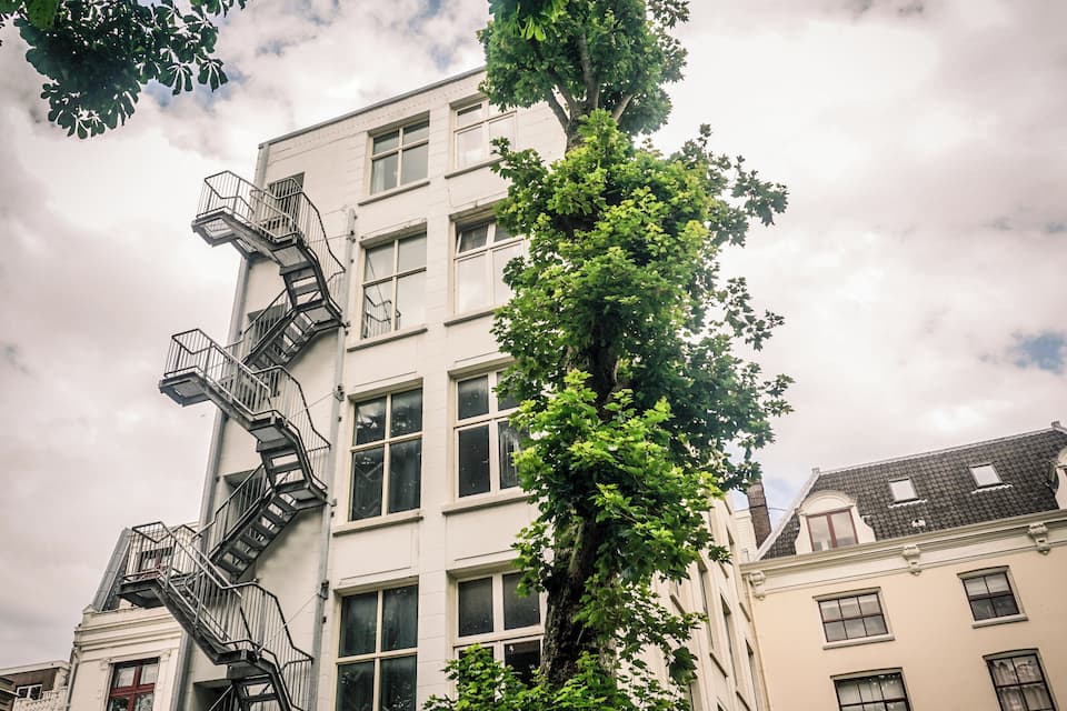 A multi-story building with a fire escape, surrounded by trees and under a cloudy sky.